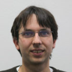 Portrait of Martin Holters, a man with short dark brown hair and glasses, smiling slightly against a plain light gray background