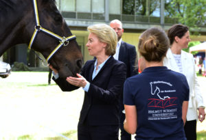 Eine blonde Dame im blauen Kostüm streichelt ein Pferd, davor steht eine junge Frau in einem blauen Polohemd mit der Aufschrift "Studentenreiter der Bundeswehr"