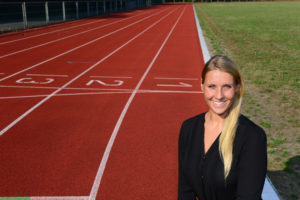 Eine junge Frau mit langen blonden Haaren steht auf einem Sportplatz.