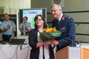 Ein Mann in der Uniform eines Luftwaffengenerals überreicht einer Frau einen bunten Blumenstrauß.