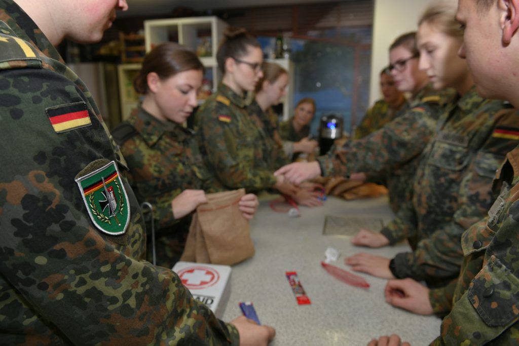 Soldatinnen und Soldaten im Flecktarnanzug hantieren in einer Küche mit Süßigkeiten und Jutebeuteln.