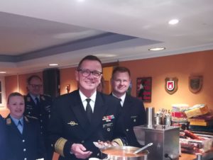 Menschen in Uniform, in der Mitte ein Admiral mit einer Bratwurst in roter Soße.