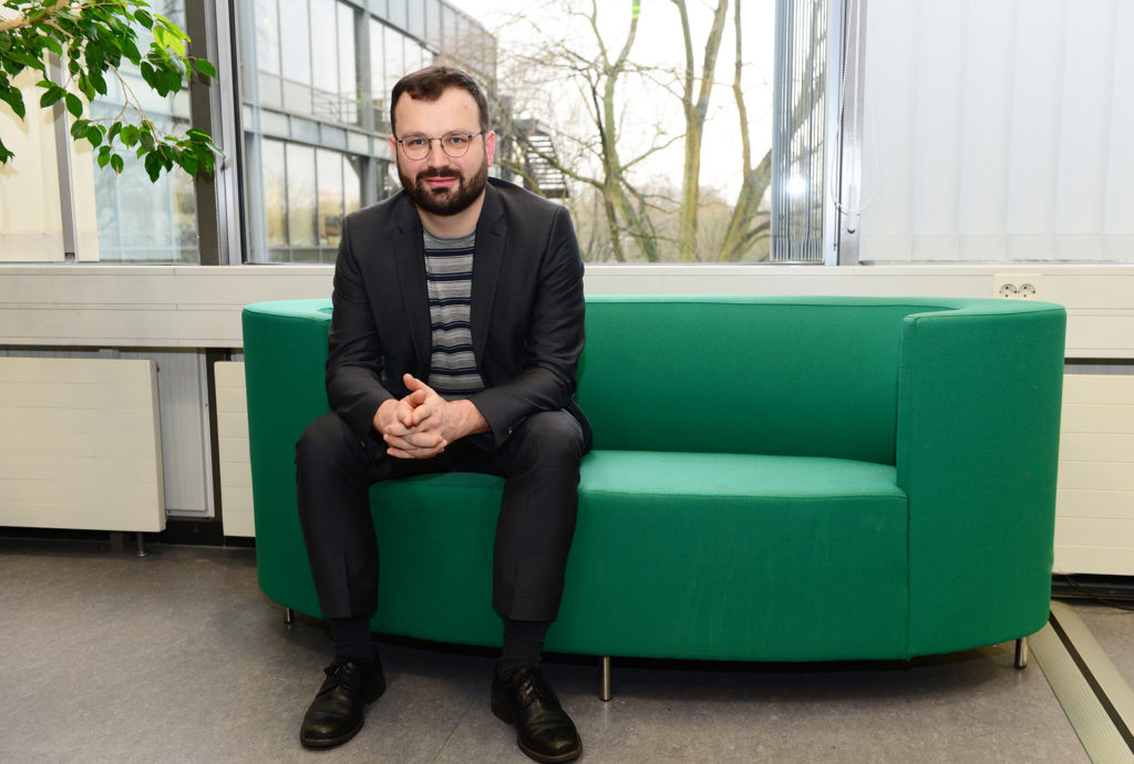 Ein Mann mit Vollbart auf einem türkisfarbenen Sofa