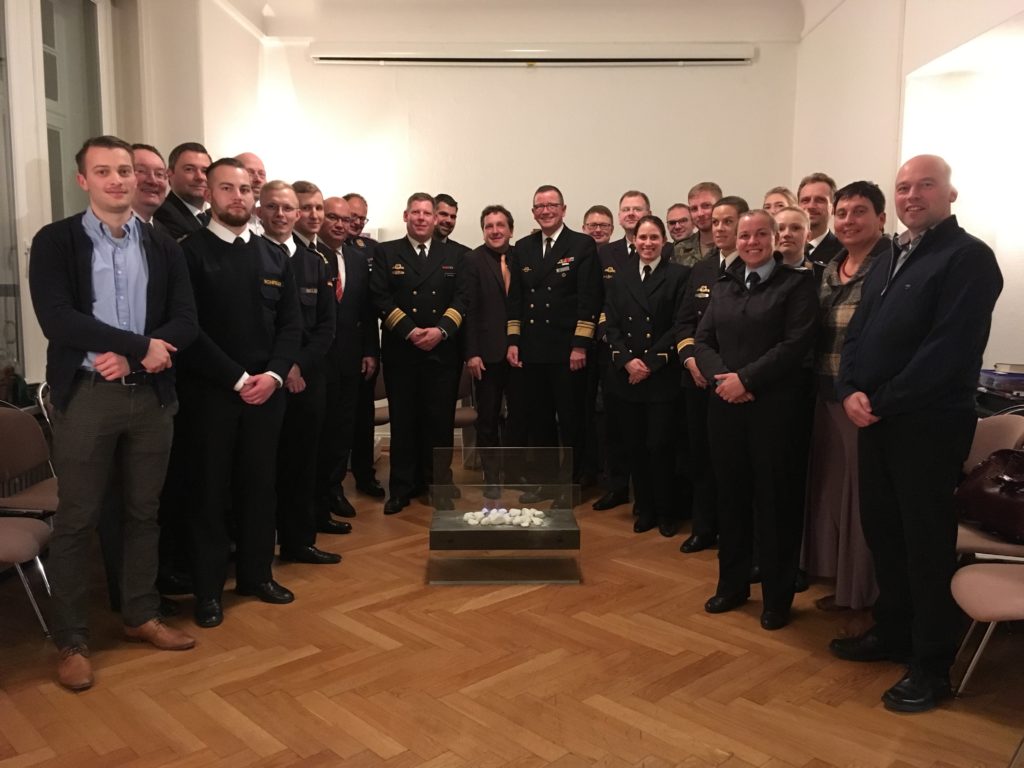 Menschen, viele davon in Marineuniform, stehen im Halbkreis um ein Ethanolfeuer herum.