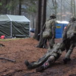 Zwei Soldaten schleifen einen dritten durch den Wald.