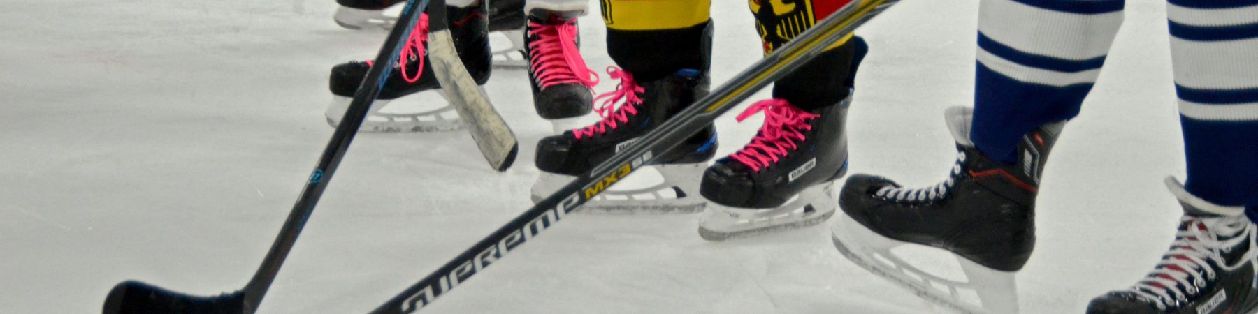 Füße in Schlittschuhen Stehen hinter Eishockeyschlägern auf einer Eisfläche