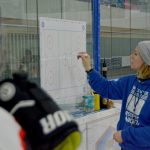 Eine Frau im blauen Kapuzenpullover zeichnet mit einem Stift auf einem Plan des Eishockey-Spielfeldes