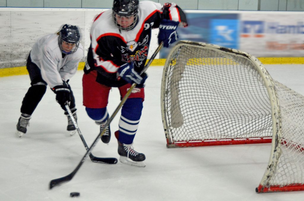 Eine Eishockeyspielerin und ein Eishockeyspieler kämpfen um einen Puck.