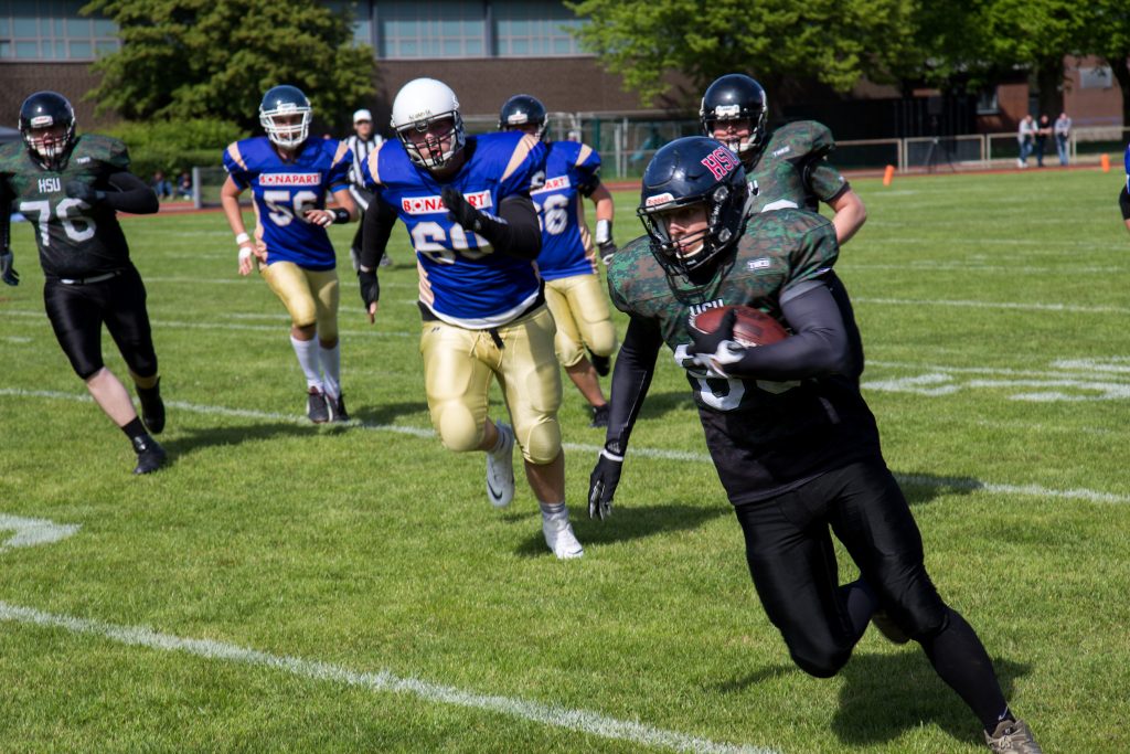 Ein Footballspieler mit dem Ball unterm Arm wird von vielen anderen verfolgt