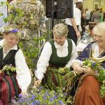 Frauen in bunten Trachten flechten Blumenkränze