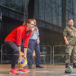 Eine Frau im Trainingsanzug wirft einen Volleyball von einer Bühne.