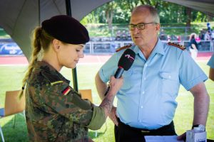 Eine Soldatin im Feldanzug hält einem Soldaten in Generalsuniform ein Mikrofon hin.