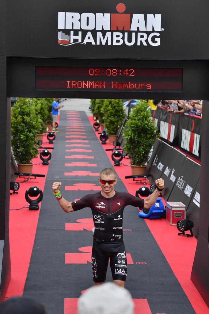 Ein Mann läuft mit Sonnenbrille durch den Zieleinlauf. Er hebt die Arme zum Jubeln.