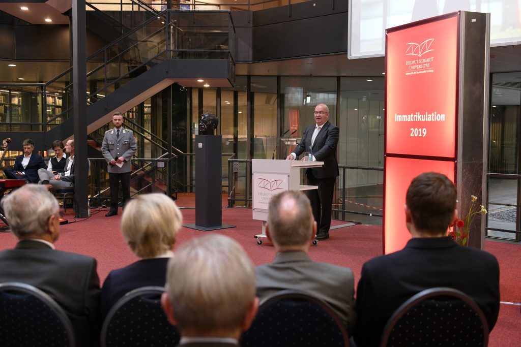 Ein Mann im grauen Anzug hiter einem Rednerpult