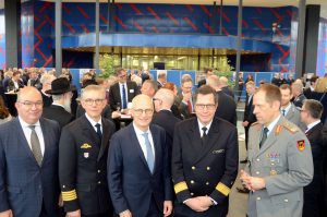 Fünf Männer, vier in Uniform stehen in einem großem Raum