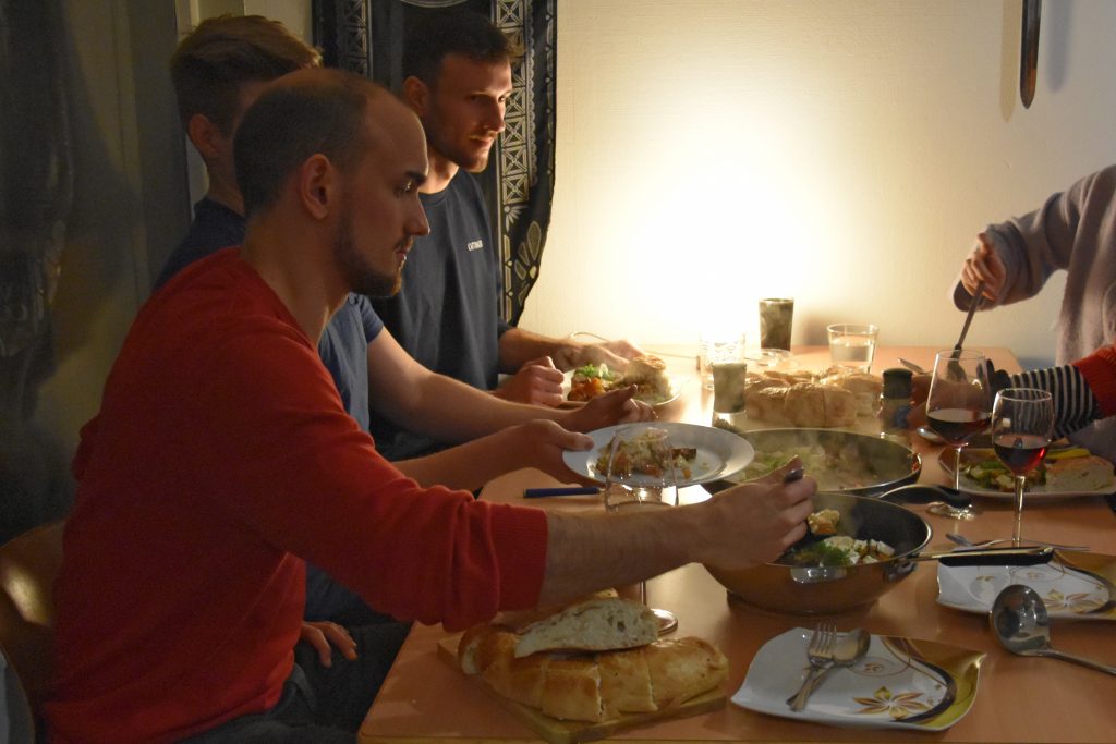 Drei junge Männer sitzen bei gedämpftem Licht an einem Tisch und essen.