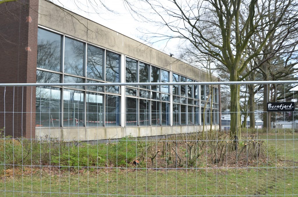 Ein Bauzaun, der die Glasfassade eine Schwimmhalle umgibt