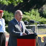 Ein Mann - es ist der Universitätspräsident - an einem Rednerpult, das mit der Bundesdienstflagge verkleidet ist. Dahinter steht ein Offizier.