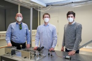 Drei junge Männer hinter einem Labortisch mit einem Laser