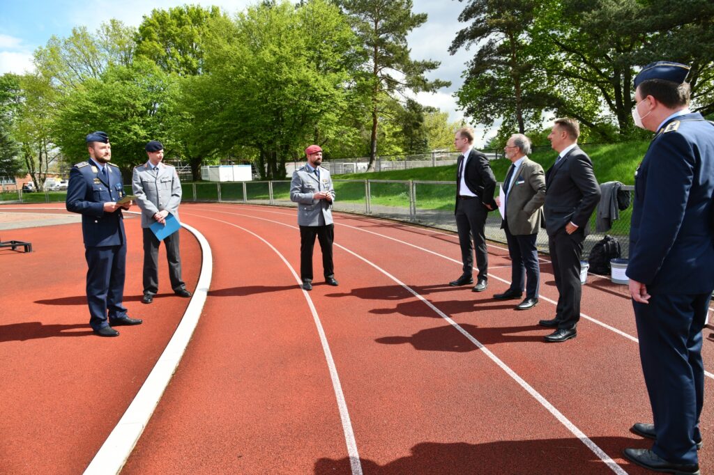 Drei Offiziere und vier Männer stehen sich auf einem Sportplatz gebenüber.