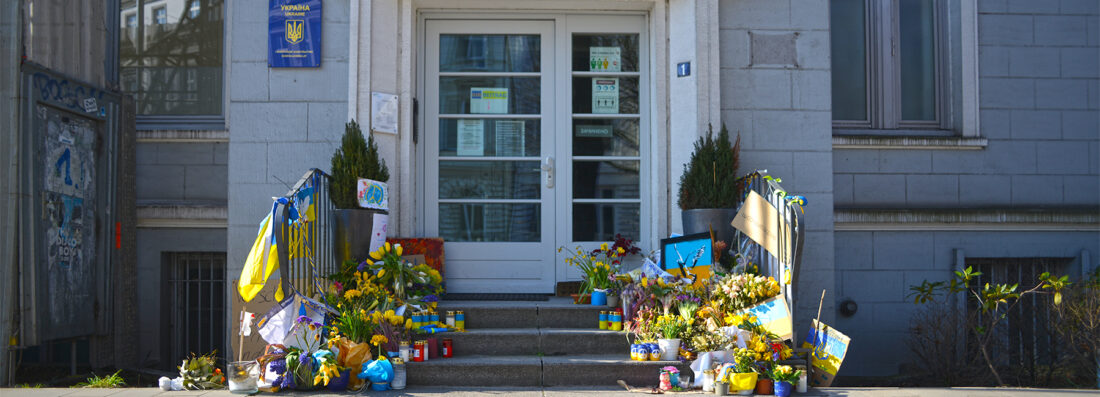 Der Eingang des ukrainischen Konsulats in Hamburg. Menschen haben Blumen, Kerzen, Flaggen und Plakate in den ukrainischen Farben Blau und Gelb aufgestellt.
