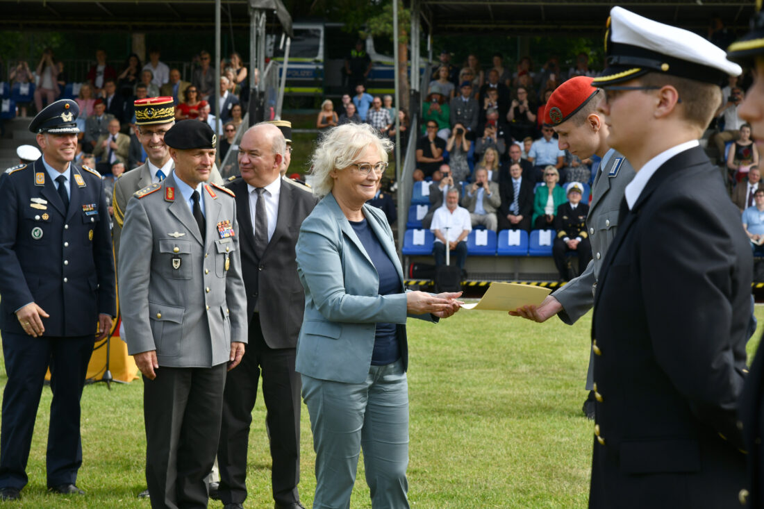 Eine Frau in einem taubenblauen Kostüm überreicht einem Soldaten eine Urkunde