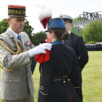 Ein französischer General steckt einer Soldatin in einer bunten Uniform Epauletten auf die Schulter