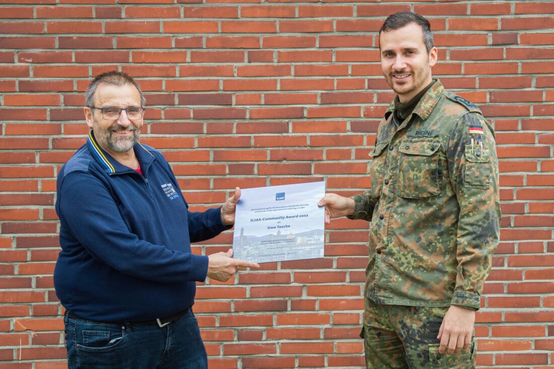 Zwei Männer, einer davon in Uniform, halten eine Urkunde