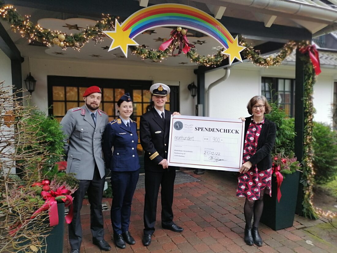 Zwei Soldaten und eine Soldatin in Uniform überreichen einen symbolischen Scheck über 900 Euro an eine Frau