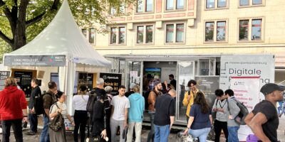 Passanten flanieren vor einem Messestand des New Production Institute anlässlich des Tages der Deutschen Einheit in Hamburg.