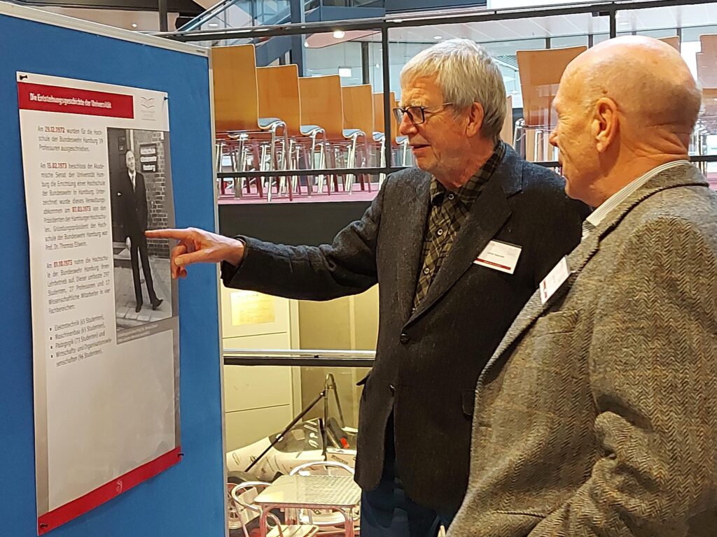 Zwei Besucher betrachten die Ausstellung zur Geschichte der HSU/UniBw H beim Alumni-Tag 2023.