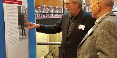 Zwei Besucher betrachten die Ausstellung zur Geschichte der HSU/UniBw H beim Alumni-Tag 2023.