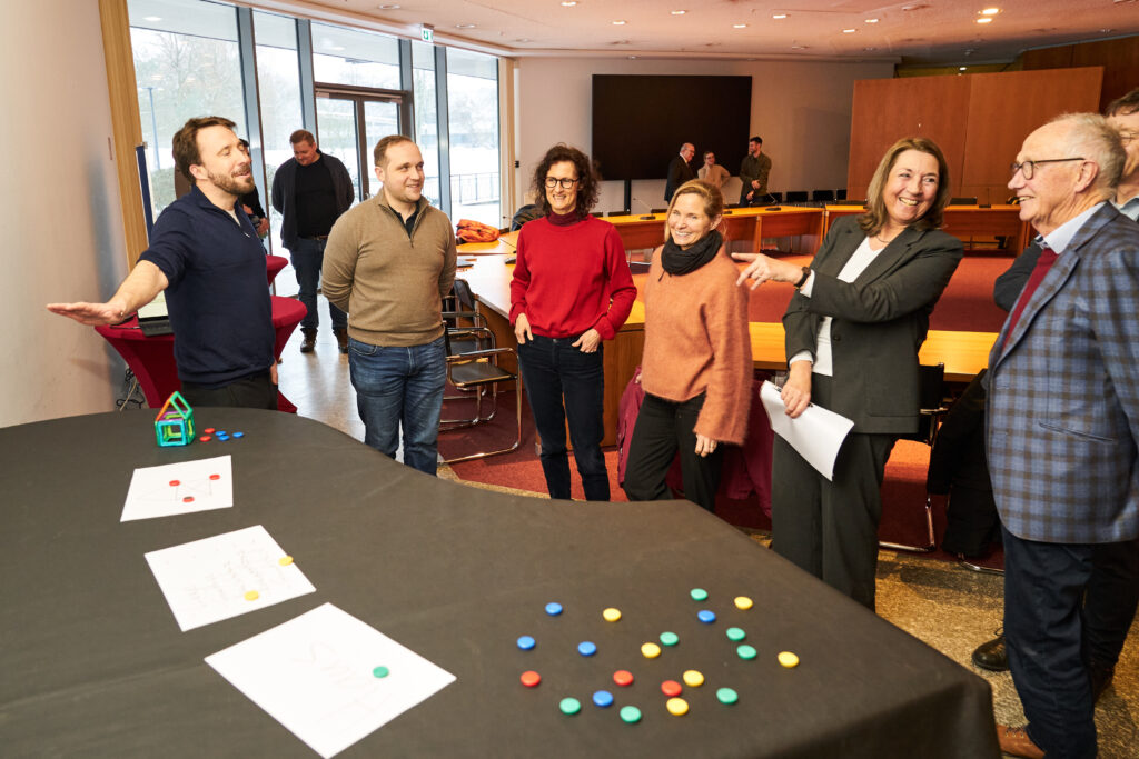 Teilnehmende diskutieren an einem Tisch mit Karten und bunten Markersteinen im Rahmen einer Wargaming‑Übung zu Entscheidungs-prozessen.