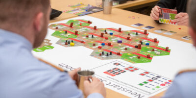 Teilnehmende führen ein Wargaming‑Szenario an einem Tisch mit Spielplan, Spielfiguren und Karten durch.