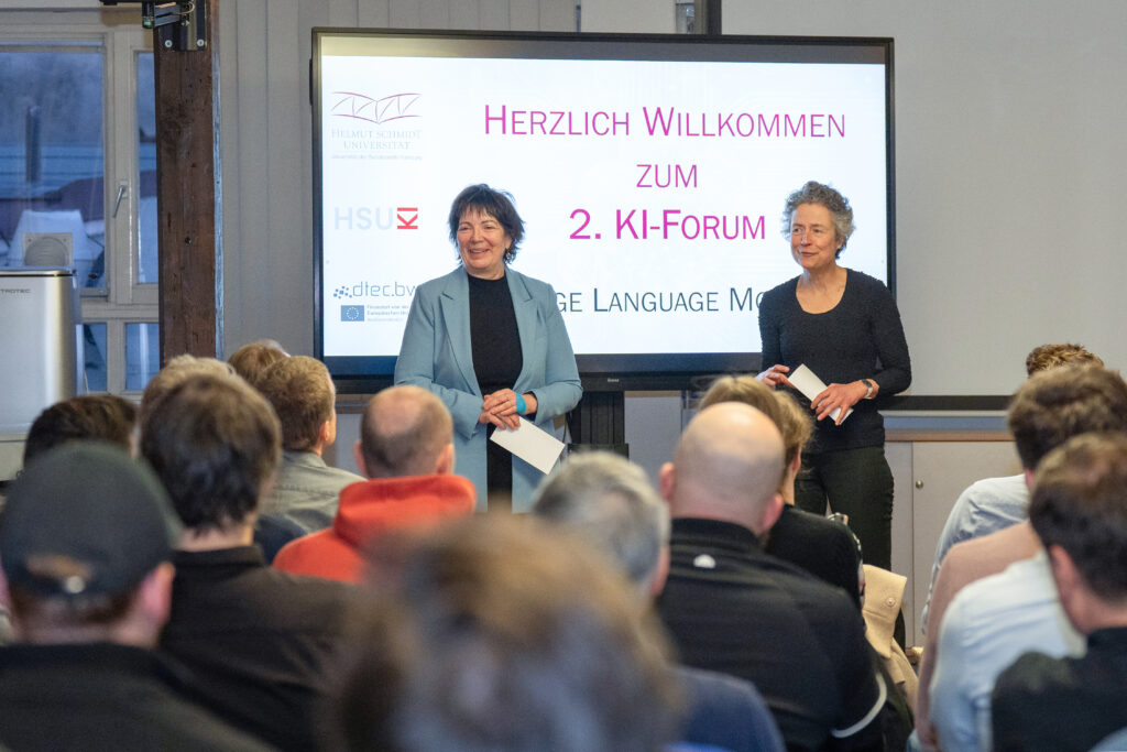 Begrüßung des Publikums beim 2. KI‑Forum vor einer Leinwand mit dem Veranstaltungstitel.