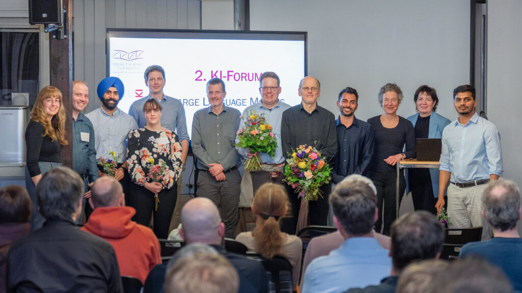 Gruppenfoto von Teilnehmenden des 2. KI‑Forums vor einer Präsentationsfolie in einem Veranstaltungsraum.