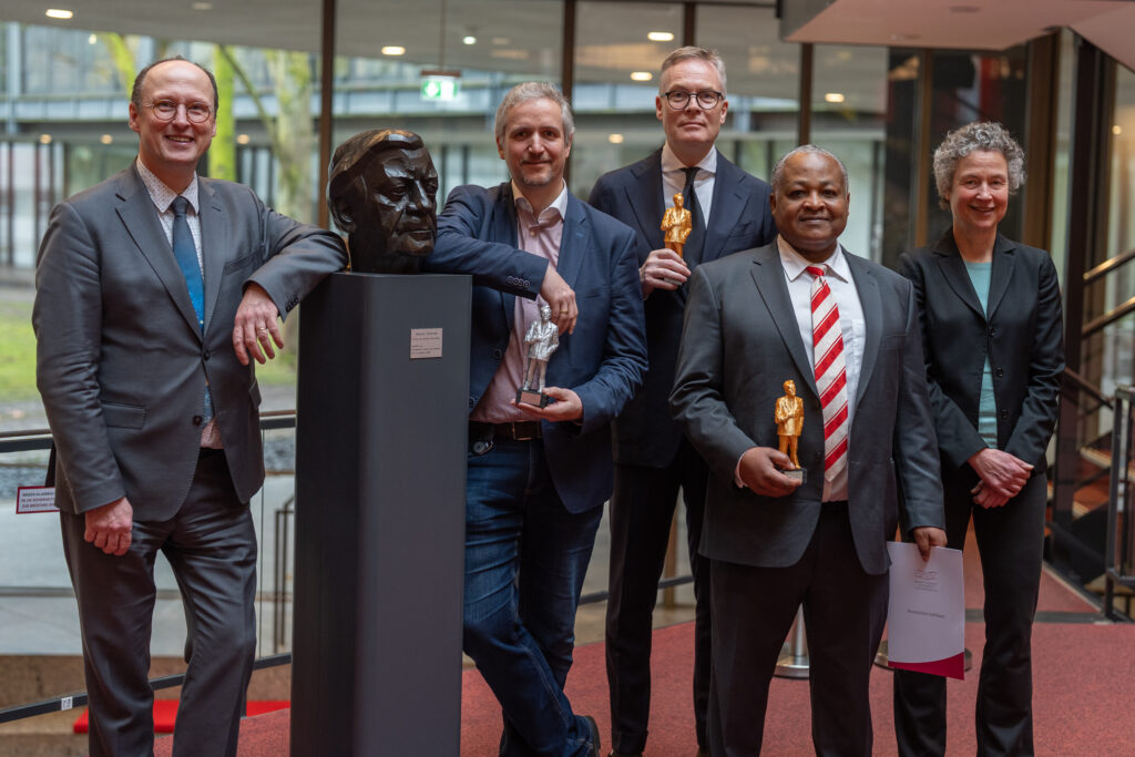 Alumni der HSU/UniBw H stehen mit Vizepräsidentin Univ.-Prof. Dr. Christina Schaefer und Vizepräsident Univ.-Prof. Dr. Thomas Klassen vor der Helmut-Schmidt-Statue der Universität.