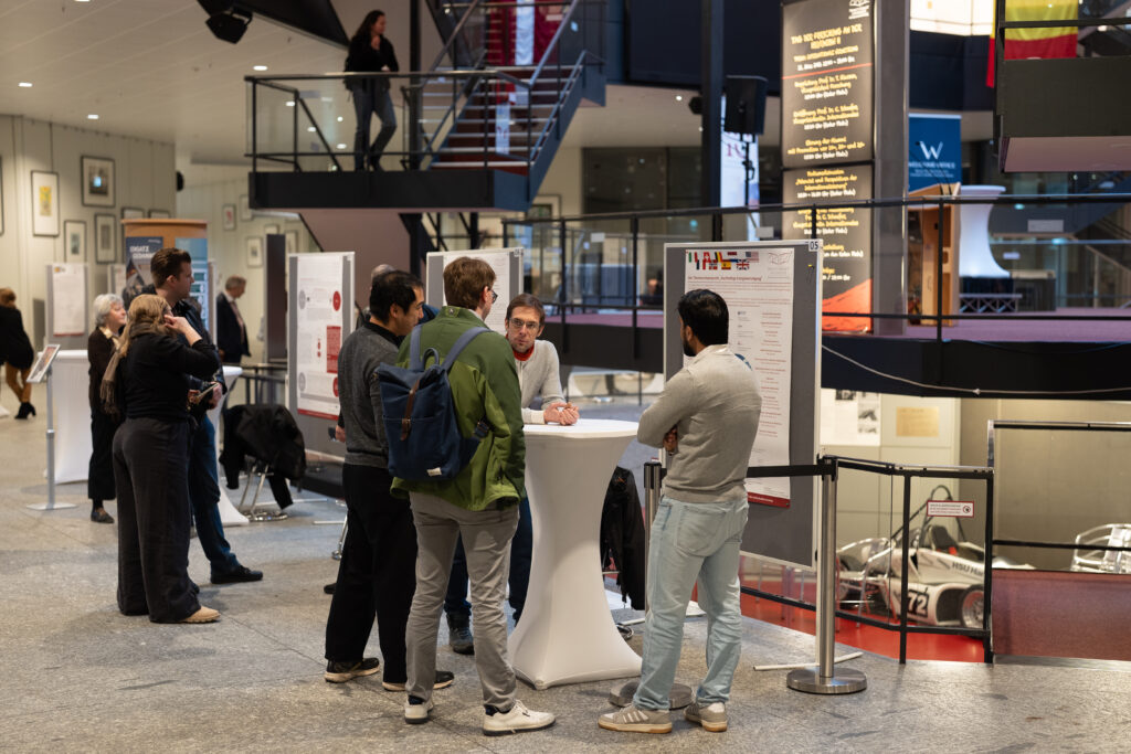 Mehrere Personen diskutieren an Stehtischen vor wissenschaftlichen Postern.
