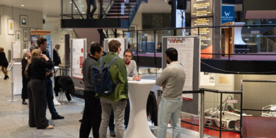 Mehrere Personen diskutieren an Stehtischen vor wissenschaftlichen Postern.