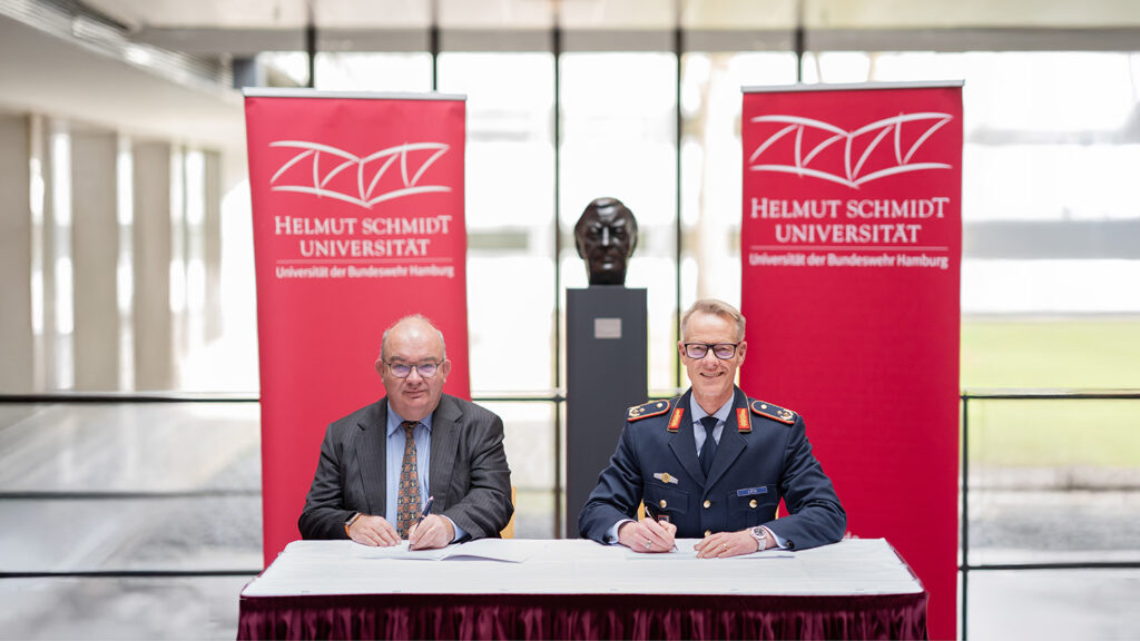 Zwei Männer sitzen an einem Tisch vor einer Helmut-Schmidt-Büste und unterzeichnen einen Vertrag.