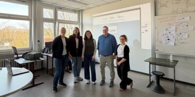 Fünf Personen stehen in einem Seminarraum der einer Schule vor einer Präsentationsfolie zu einem Innovations‑ oder Qualifizierungsprojekt.