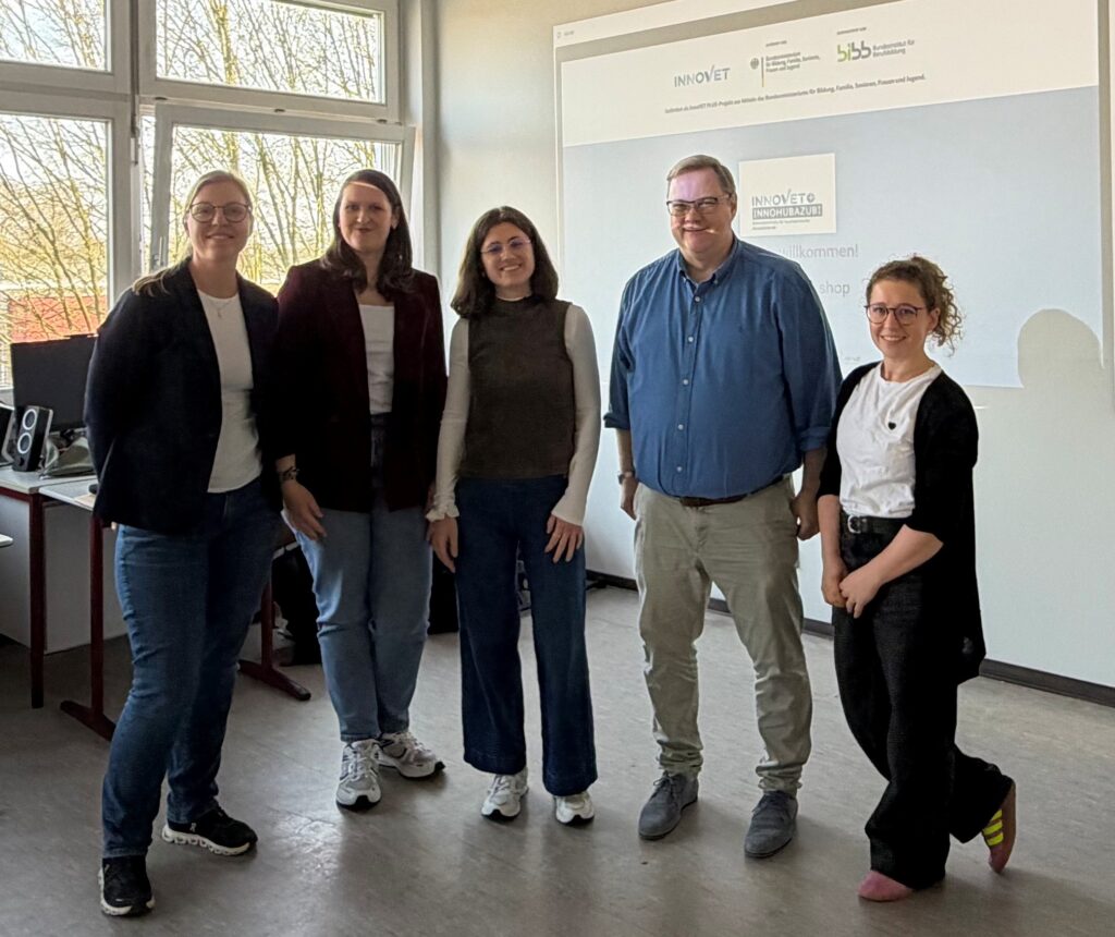 Fünf Personen stehen in einem Seminarraum der einer Schule vor einer Präsentationsfolie zu einem Innovations‑ oder Qualifizierungsprojekt.