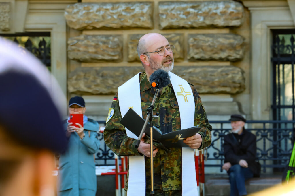 Pater Henrich hält vor dem Rathaus eine Ansprache an einem Mikrofon.