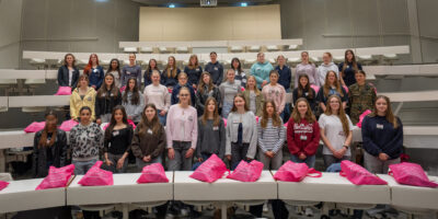 Große Gruppe von Schülerinnen steht in einem Hörsaal der Helmut‑Schmidt‑Universität/Universität der Bundeswehr Hamburg, vor ihnen liegen pinke Stofftaschen mit Universitätslogo.