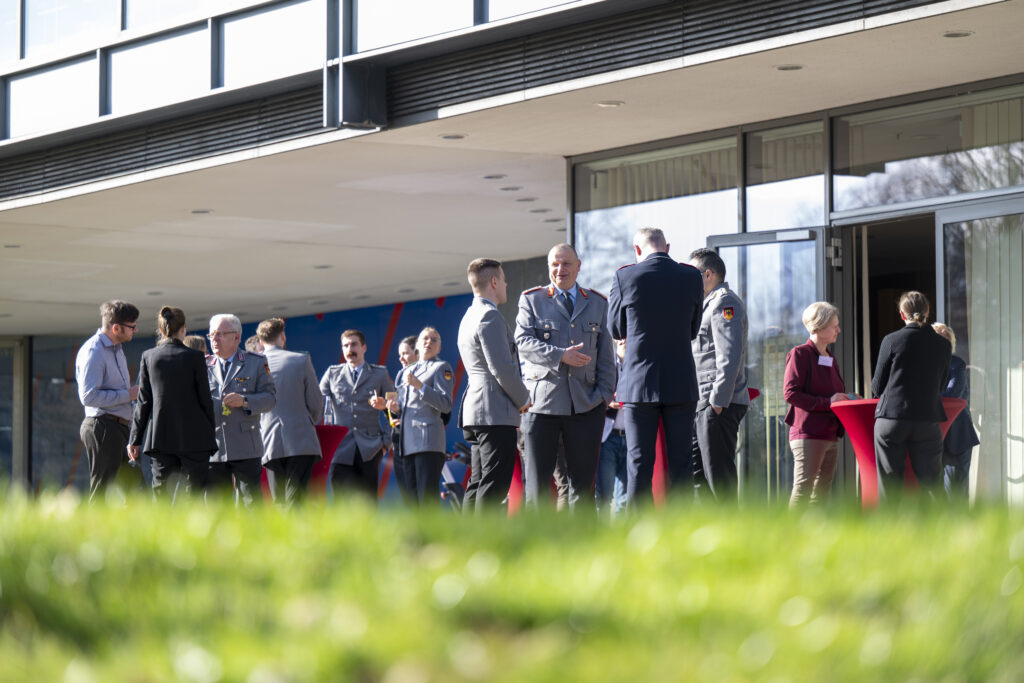 Menschen in Uniformen stehen im vor einem Gebäude und Unterhalten sich.