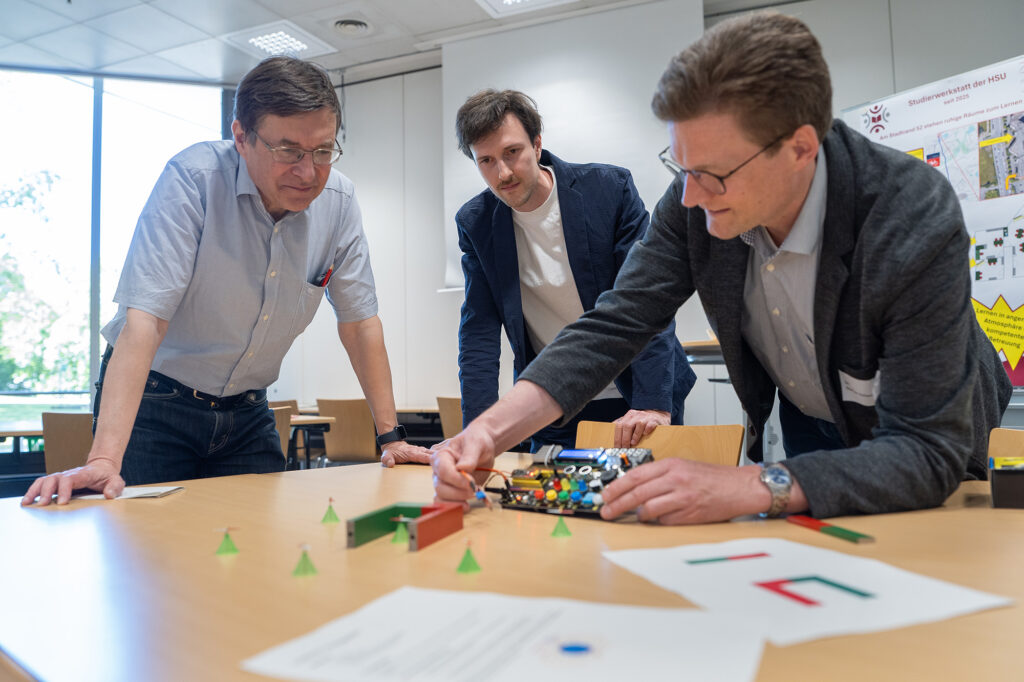 Mehrere Teilnehmende arbeiten gemeinsam an einem elektronischen Aufbau während eines Workshops.
