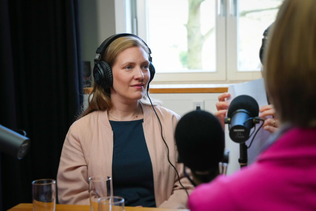 Person mit Kopfhörern spricht in ein Mikrofon in einem Podcast‑Studio.