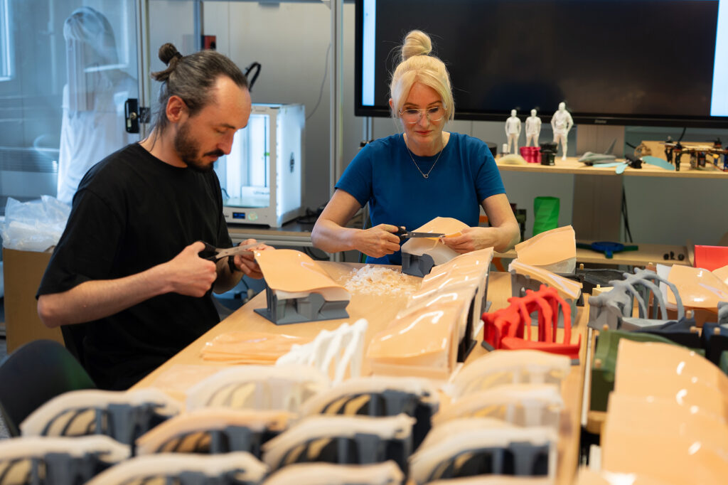 Zwei Personen schneiden im Labor Silikonmaterial für Trainingsmodelle; auf dem Tisch liegen mehrere Modellbauteile.