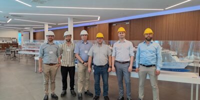 Sechs Teilnehmende des Forschungsprojekts H2MASS stehen während eines Kick-off-Workshops in einer Ausstellungshalle der MEYER WERFT vor mehreren Modellen von Passagierschiffen. Einige der Beteiligten tragen Schutzhelme. Im Hintergrund sind Vitrinen mit Schiffsmodellen zu sehen.