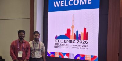 Zwei wissenschaftliche Mitarbeiter der Professur für Data Engineering stehen vor einer digitalen Anzeigetafel der IEEE Engineering in Medicine and Biology Conference (EMBC) 2026 in Toronto. Die Konferenzanzeige zeigt das Logo der Veranstaltung sowie Veranstaltungsort und -datum.
